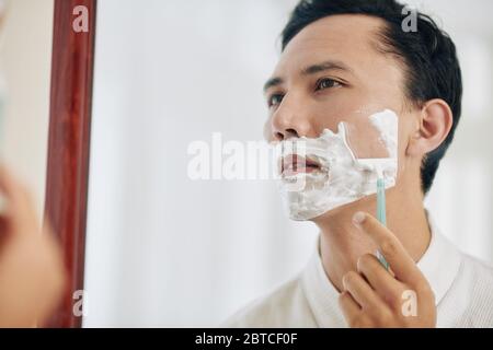 Homme de course mixte se rasant devant le miroir après avoir pris une douche le matin Banque D'Images