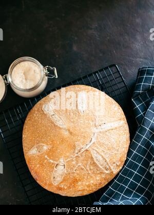 Pain au levain rond de blé et entrée de levain dans un pot en verre. Vue de dessus de délicieux pain de levain maison sur fond noir avec espace de copie. Concept de fabrication de pain au levain fait maison. Verticale. Banque D'Images