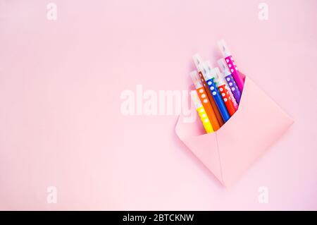 Enveloppe rose papier pleine de marqueurs colorés sur fond rose pastel avec espace de copie. Banque D'Images