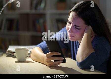 Triste femme se plaignant de vérifier un smartphone assis la nuit dans le salon à la maison Banque D'Images