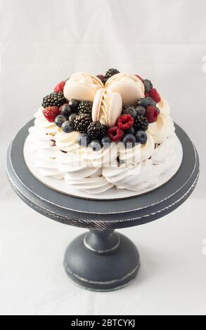 Gâteau Pavlova à la meringue, crème fouettée et baies fraîches. Décoration avec macarons vanille. Fond blanc Uni. Copier l'espace. Banque D'Images