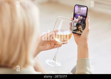 Vue arrière d'une femme qui parle en ligne avec ses amis sur un téléphone portable et qui boit du vin qu'elle célèbre pour ses vacances Banque D'Images