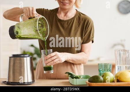 Gros plan de la femme qui verse le jus du blender dans le verre et le boit le matin Banque D'Images