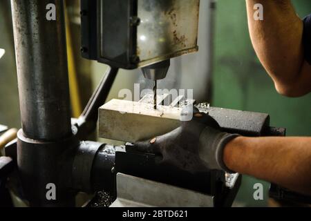 Un ouvrier fore un bloc d'aluminium sur une grande perceuse de table industrielle dans un atelier en gros plan sur ses mains gantées Banque D'Images