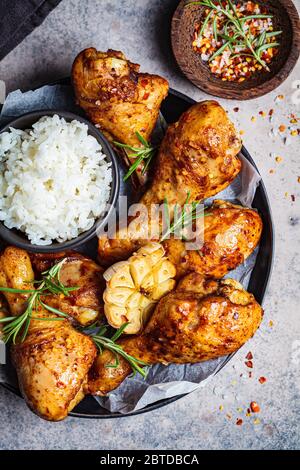 Frit des cuisses de poulet épicées avec du riz, de l'ail et des herbes dans une assiette noire, fond sombre. Banque D'Images