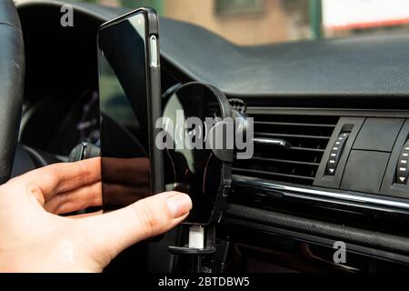 Une main féminine met un téléphone moderne sur une charge rapide sans fil dans la voiture. Banque D'Images