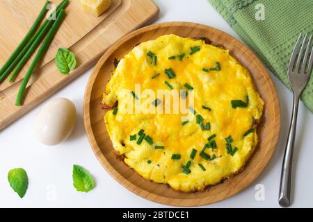 Omelette moelleuse d'œufs fouettés avec fromage cheddar et oignons verts saupoudrés dans une assiette en bois. Banque D'Images