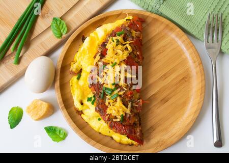 Omelette aux œufs pliée et moelleuse avec tomate, poivron rouge, ail, échalotes et cheddar dans une assiette en bois. Banque D'Images