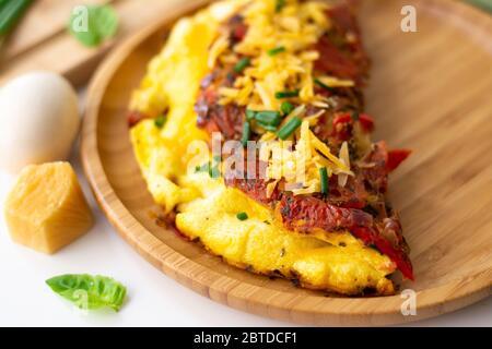 Omelette aux œufs pliée et moelleuse avec tomate, poivron rouge, ail, échalotes et cheddar dans une assiette en bois. Banque D'Images