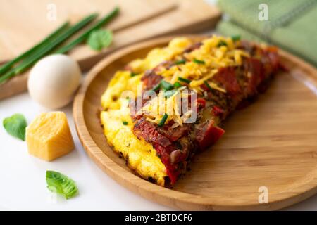 Omelette aux œufs pliée et moelleuse avec tomate, poivron rouge, ail, échalotes et cheddar dans une assiette en bois. Banque D'Images