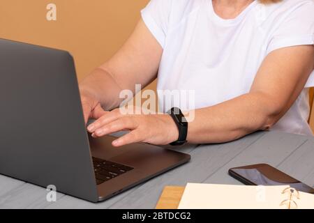 Gros plan d'une femme assise devant son ordinateur portable, téléphone à la table et mains au clavier dans la pièce Banque D'Images