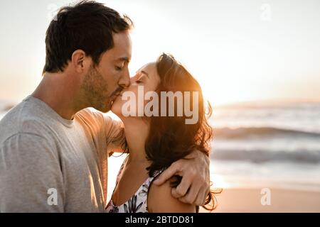 Un jeune couple aimant embrassant sur une plage au coucher du soleil Banque D'Images