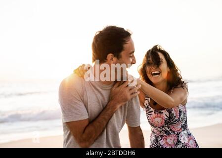 Couple riant s'amuser ensemble sur une plage au coucher du soleil Banque D'Images