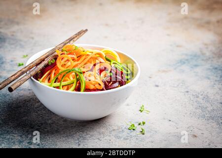 Nouilles aux légumes - courgettes, betteraves et carottes dans un bol, fond sombre. Aliments végétaliens crus. Banque D'Images