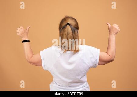 Femme en t-shirt blanc vierge debout à l'arrière de l'appareil photo avec les mains levées, en tenant les pouces vers le haut Banque D'Images