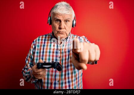 Senior beau joueur de hary homme jouant le jeu vidéo en utilisant le joystick et les écouteurs pointant avec le doigt vers l'appareil photo et à vous, signe de main, un positif Banque D'Images