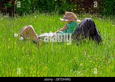 Personne grand-père couché dans prairie herbe longue pelouse tenant bébé Port de chapeau de paille au printemps Mai jardin 2020 Carmarthenshire pays de Galles R.-U. KATHY DEWITT Banque D'Images