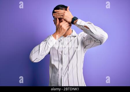 Jeune homme hispanique élégant portant un élégant chemise d'affaires debout sur fond violet couvrant les yeux et la bouche avec les mains, surpris et choqué. Banque D'Images