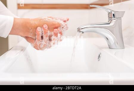 Homme ou femme se lave les mains avec du savon tout en se tenant au lavabo dans la salle de bains. Banque D'Images