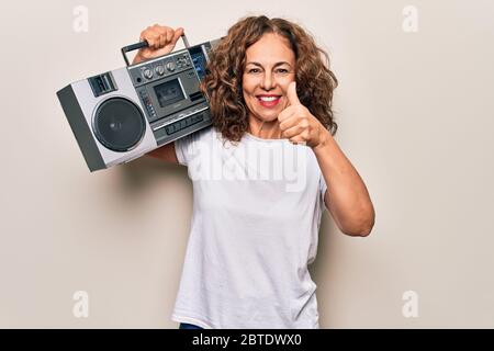 Âge moyen brunette hipster femme tenant la boombox de musique rétro sur fond isolé sourire heureux et positif, pouce vers le haut faisant excellent et approv Banque D'Images