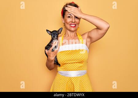 Âge moyen senior épingler une femme portant la robe rétro style 50s tenant chien chihuahua stressé avec main sur la tête, choqué par la honte et le visage surprise, a Banque D'Images