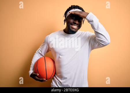 Un jeune sportif américain d'afrique qui fait du sport tient le ballon de basket-ball sur fond jaune, stressé de main sur la tête, choqué par la honte et surpris Banque D'Images