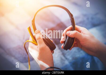 L'homme tient de grands écouteurs jaunes avec un microphone, éclairé par la lumière du soleil, et est sur le point de les mettre sur. Musique et inspiration. Banque D'Images