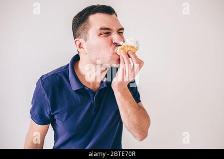 Jeune homme isolé sur fond blanc. Guy mangeant de la graisse délicieux gâteau avec de la crème sur lui. Homme affamé mâchant avec plaisir Banque D'Images