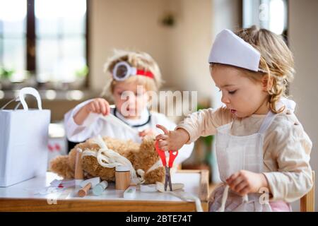 Deux petits enfants avec des uniformes de médecin à l'intérieur à la maison, jouant. Banque D'Images