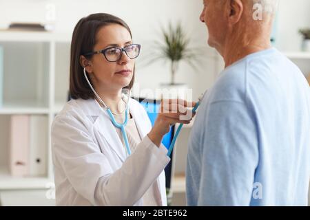 Portrait de la femme médecin à la taille, écoutant le cœur et la respiration du patient âgé, en plaçant le stéthoscope sur la poitrine pendant la consultation en clinique Banque D'Images