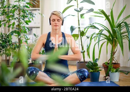 Vue de face d'une jeune femme à l'intérieur à la maison, faisant de l'exercice de yoga. Banque D'Images