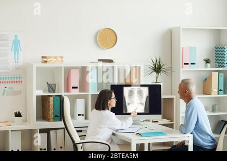 Vue latérale grand angle chez la femme médecin, montrant une image radiographique des poumons et de la poitrine, tout en consultant un patient senior en clinique, espace de copie Banque D'Images