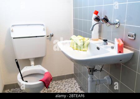 Une vue verticale d'une salle de bains simple et ancienne carrelée et des toilettes avec divers produits de nettoyage Banque D'Images