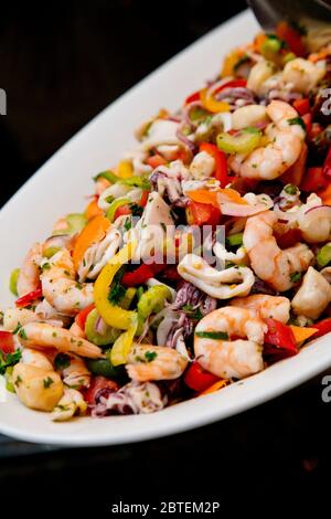 Buffet de fruits de mer lors de la célébration de l'événement. Salade de fruits de mer mixée et cuite sur un grand plateau blanc qui attend le service des clients. Banque D'Images