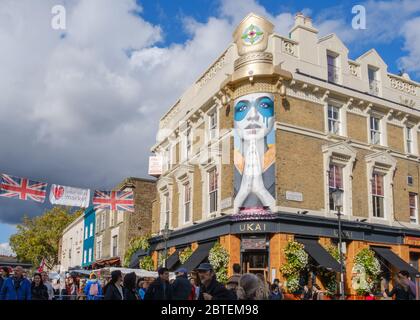 Une foule de gens magasinent au marché de Portobello Road avec le restaurant japonais Ukai et l'art de rue mural Lady Kinoko de fin DAC en arrière-plan. Banque D'Images