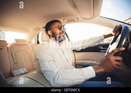 Un homme africain conduit sa propre voiture neuve assis sur son siège Banque D'Images