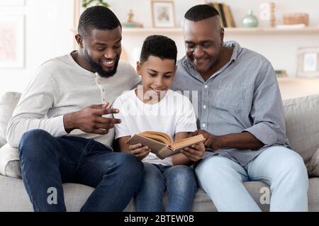 Livre de lecture de garçon de préadolescence en Afrique souriante avec papa et grand-père à la maison Banque D'Images