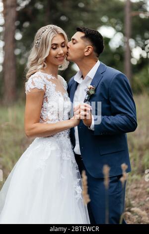 Marié embrassant la mariée souriante à l'arrière-plan des arbres Banque D'Images