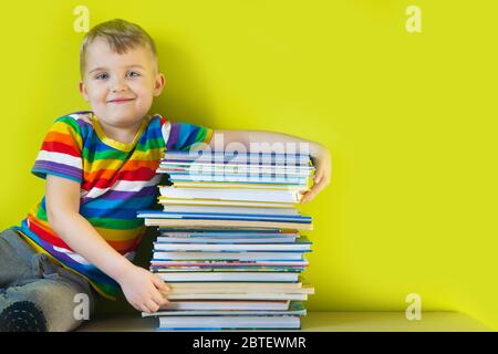 L'enfant tient une grande pile de livres d'enfants dans ses mains. Arrière-plan vert. Banque D'Images