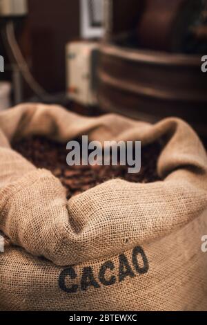 Sac de jute plein de fèves de cacao dans un atelier de chocolaterie, avec l'équipement de conchage et de mélange sur le fond Banque D'Images