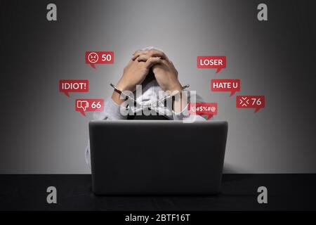 concept de cyber-intimidation. Un menotté est accusé d'être un défendeur social, se pliant la tête devant l'ordinateur portable avec des discours de haine comme Banque D'Images