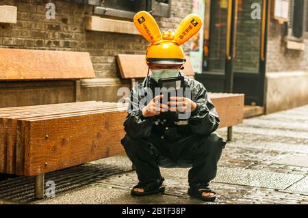 Un employé de Meituan Dianping se croche en utilisant son téléphone en attendant son prochain emploi dans le quartier branché de Xintiandi à Shanghai. Banque D'Images