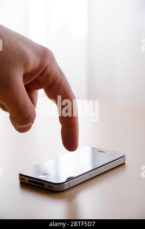 Gros plan de la main d'un homme tenant et touchant ou utilisant le smartphone iPhone 4s sur un bureau en bois sur un arrière-plan blanc lumineux avec espace de copie Banque D'Images