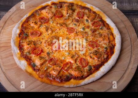 Pizza au saumon, aux tomates et aux câpres sur une planche de bois. Pizza entière. Gros plan. Banque D'Images