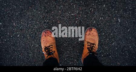 Zénith vue des pieds d'une personne portant des bottes en cuir brun mouillé sur le sol d'une route. Banque D'Images