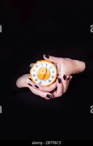 Les femmes tiennent le minuteur de cuisine orange sur fond noir. Copier l'espace. Concept de temps Banque D'Images