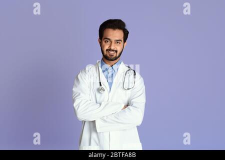 Médecin indien confiant en uniforme croisant ses bras sur fond de couleur Banque D'Images