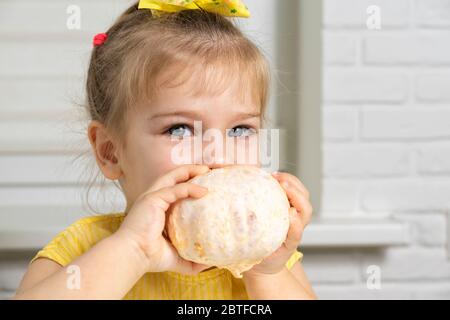 une petite fille dans un chemisier jaune s'assoit à une table dans la cuisine, sourit un pamplemousse pelé dans ses mains. agrumes dans la nutrition des enfants Banque D'Images