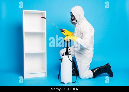 Profil complet de corps photo de côté de l'homme en costume blanc noisette laver nettoyer désinfecter la surface des étagères de l'épidémie de covid utiliser l'équipement de pulvérisation Banque D'Images