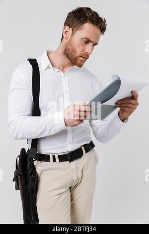Image d'un jeune homme concentré tenant une planchette à pince et lisant des documents isolés sur fond blanc Banque D'Images